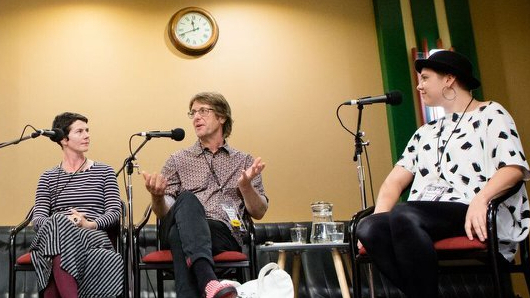 A panel of three people sitting and speaking to one another.